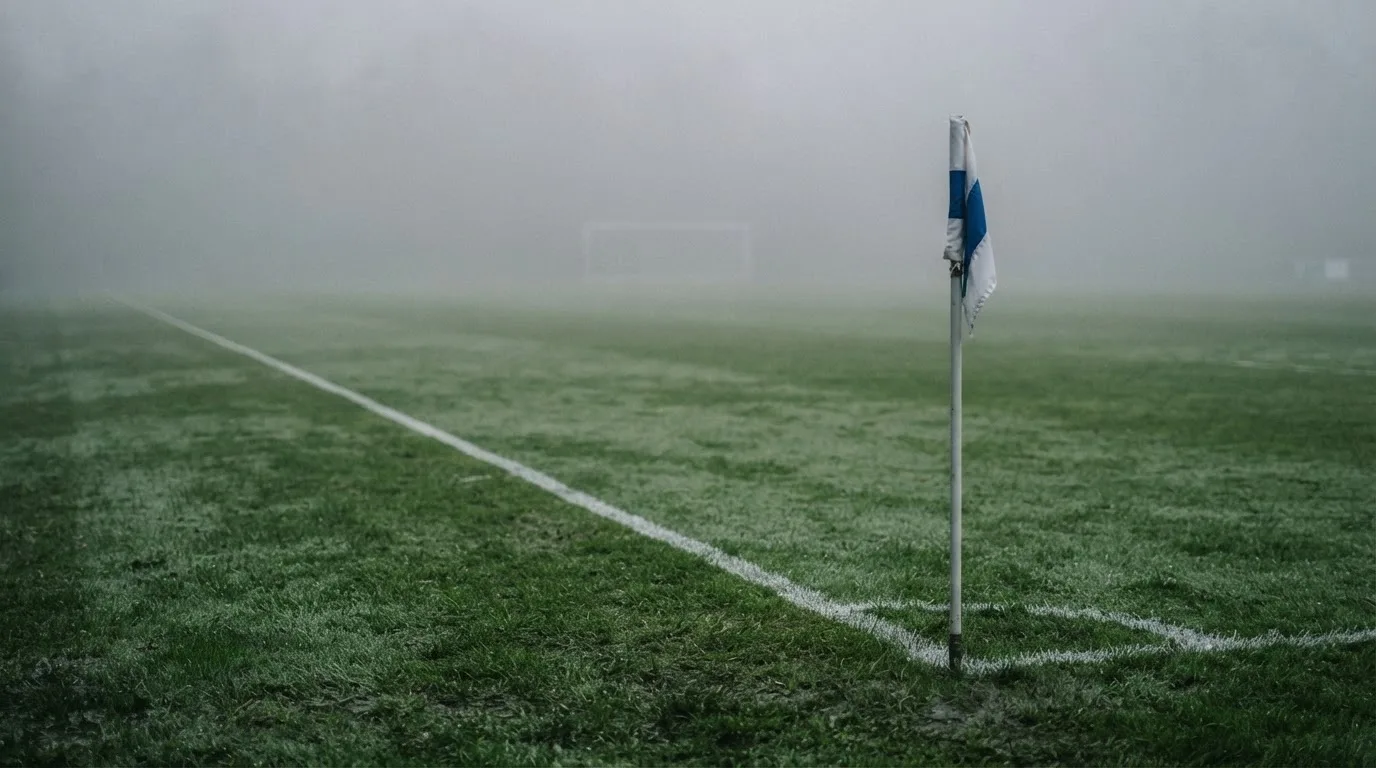 Der Rand eines Spielfelds mit weißer Linie und Eckfahne bei Nebel am frühen Morgen, ohne Menschen.