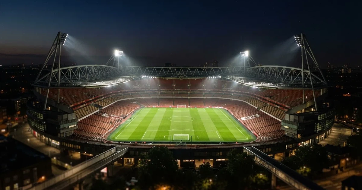 Ein großes Stadion bei Nacht, aus der Ferne unter Flutlicht gesehen, die Ränge hell erleuchtet, der Rasen leuchtend grün.