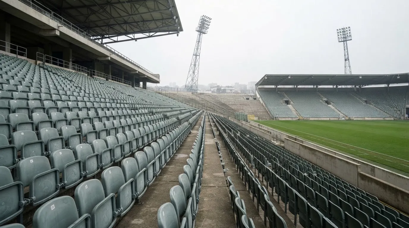 Eine leere Tribüne eines Fußballstadions bei Tageslicht, Sitzschalen in Reihen und dahinter ein Flutlichtmast.