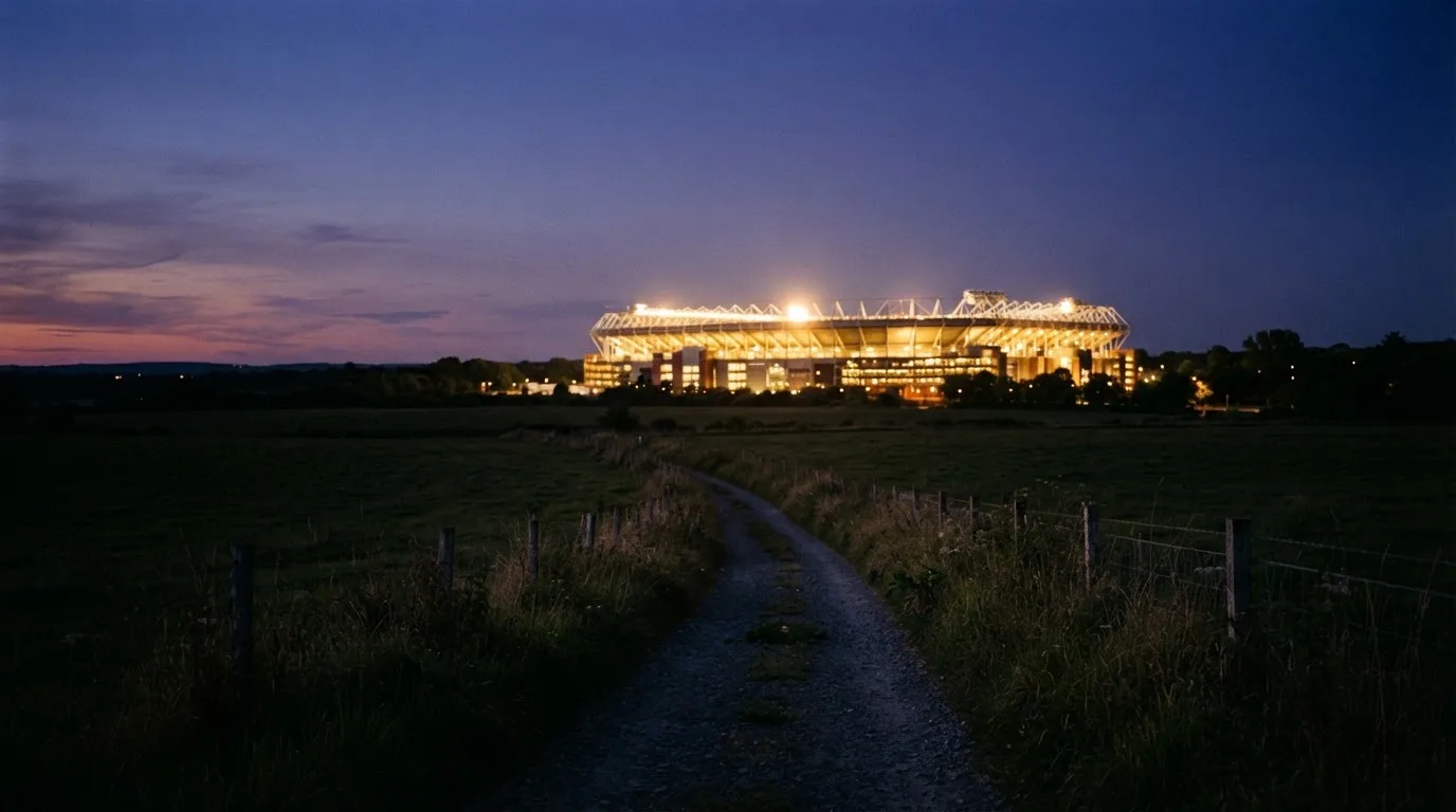 Ein beleuchtetes Stadion aus großer Distanz am Abend, im Vordergrund ein Feldweg.