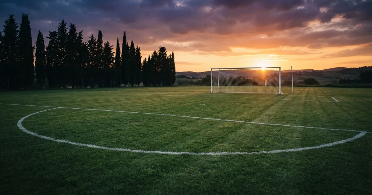 Ein Fußballtor mit Netz auf einem leeren Platz im Abendlicht, der Rasen frisch gemäht, im Hintergrund Zypressen.