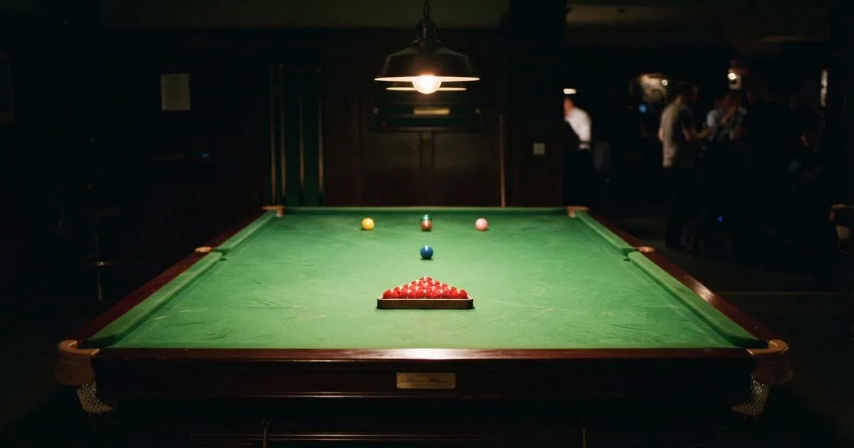 Ein Snookertisch mit grünem Tuch und aufgebauten roten Kugeln in einem abgedunkelten Raum unter einer hängenden Lampe.